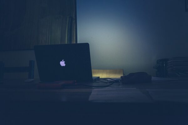 Un ordinateur Apple dans le noir avec juste le logo sur le clapet qui est lumineux
